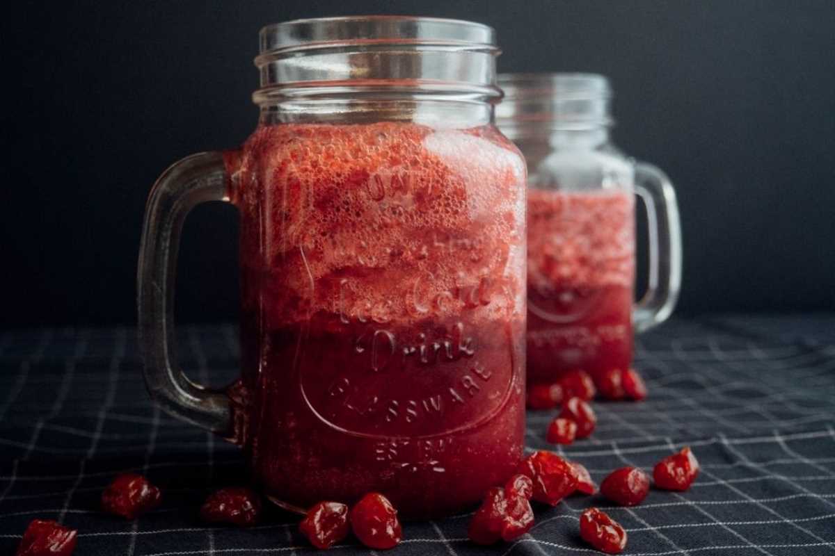 Two mason jars filled with freshly squeezed cranberry juice, surrounded by whole cranberries
